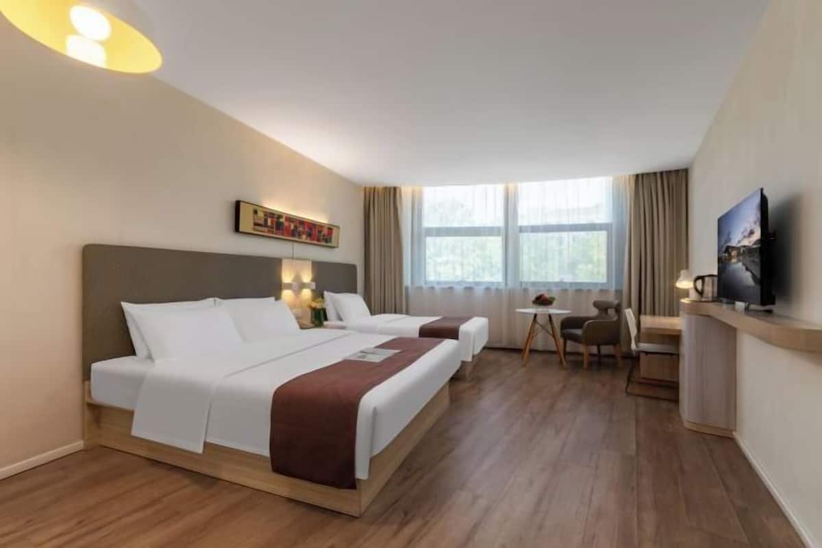 A hotel room with two beds, a desk, a chair, a television, and a window with curtains.