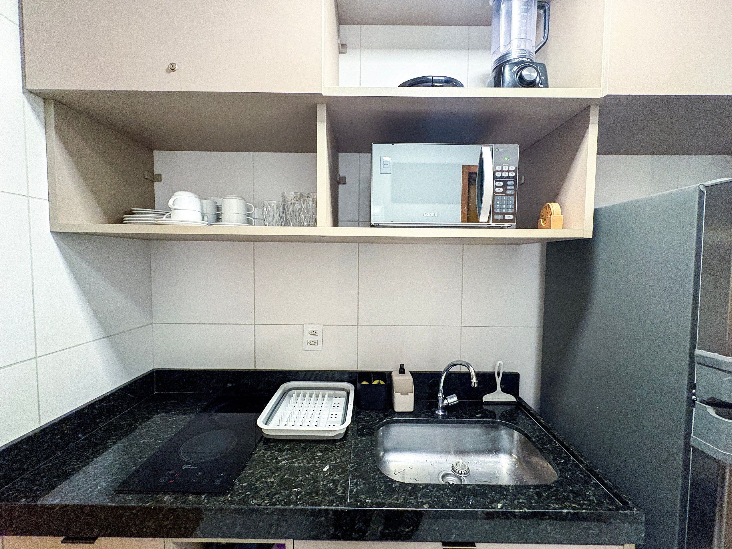 A kitchen with a black granite countertop, a built-in sink, a microwave, and a blender on the countertop.