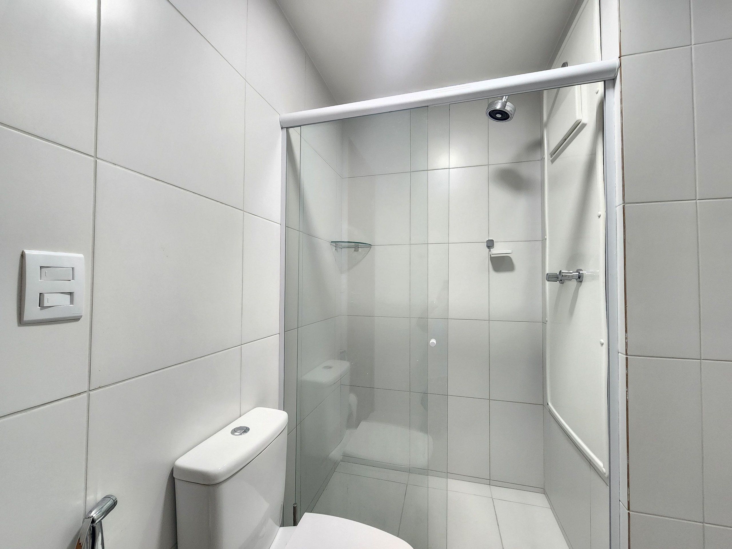 Un baño moderno con azulejos blancos, cabina de ducha de cristal, inodoro y panel de control de la ducha.
