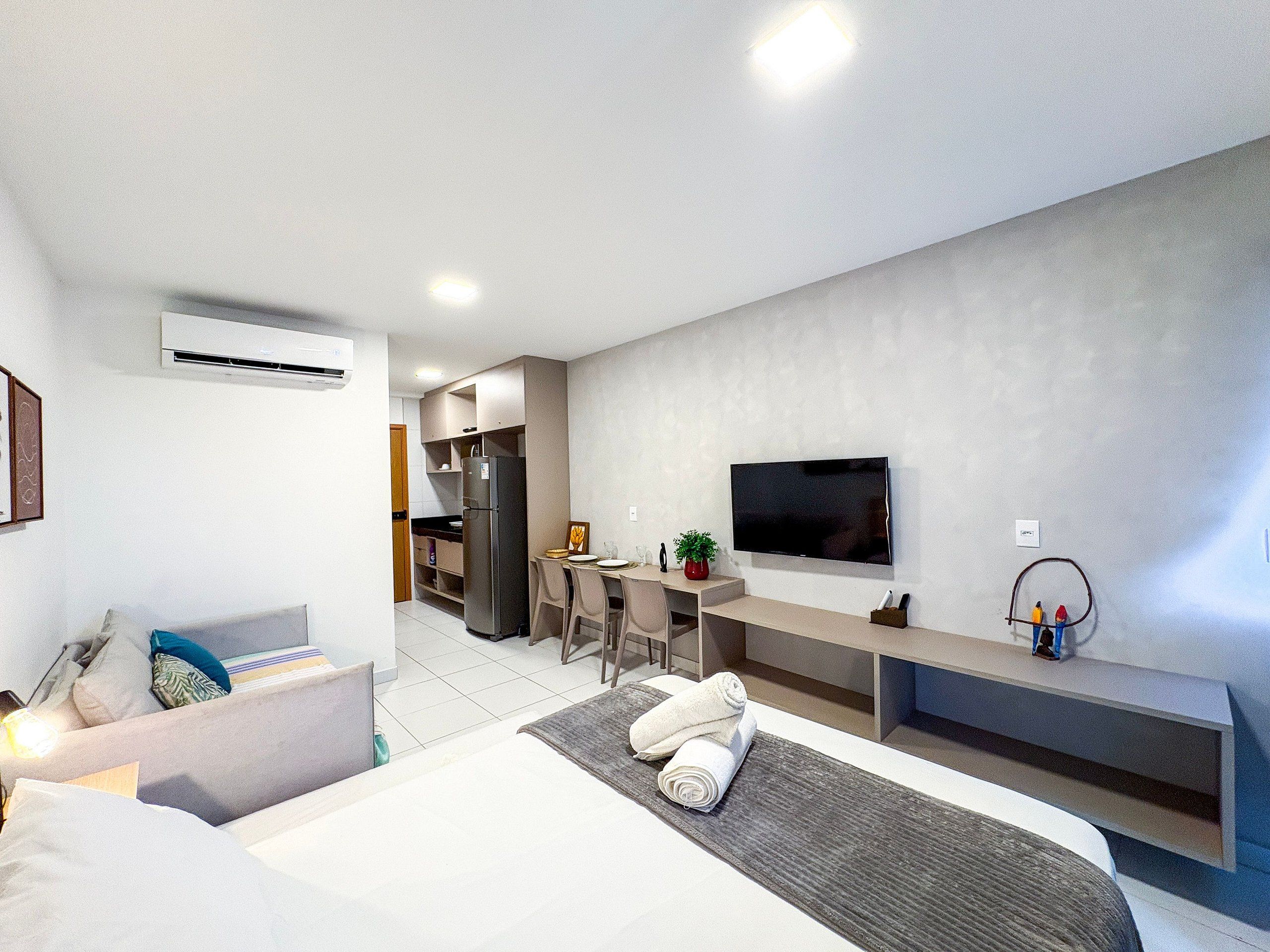 Une chambre d’hôtel moderne avec un lit, un bureau, une télévision et, au fond, une petite cuisine.