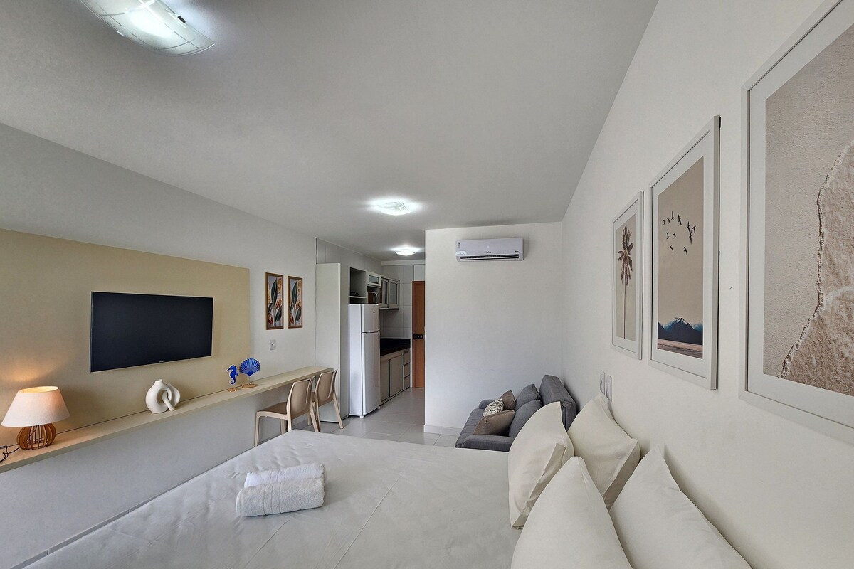 A hotel room with a bed, a TV, a desk, and a kitchenette.