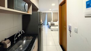 Une cuisine d’hôtel moderne équipée d’un four à micro-ondes encastré, d’un évier en acier inoxydable et d’un réfrigérateur.