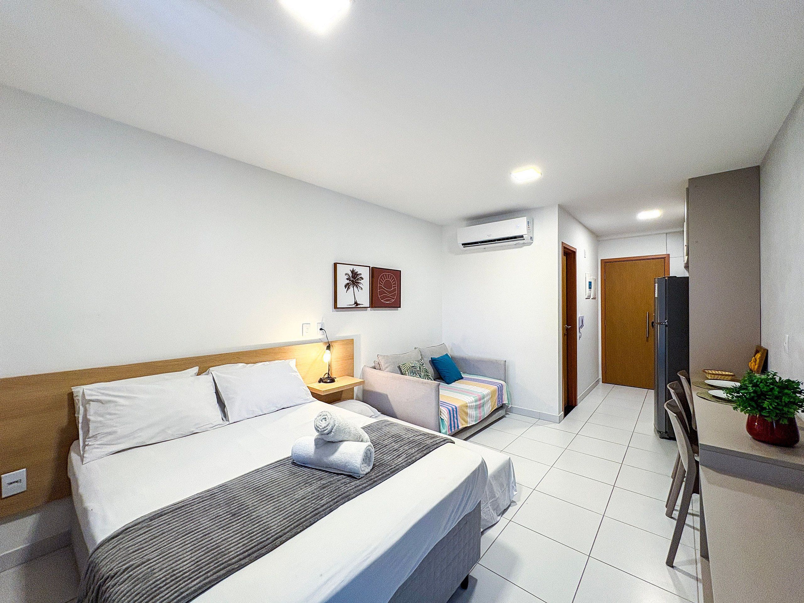 Ein Hotelzimmer mit Bett, Nachttisch, Lampe, Klimaanlage und einer kleinen Sitzecke mit Sessel und Kissen.