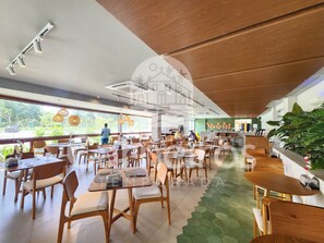 A spacious restaurant with wooden furniture, large windows, and a green-tiled floor.