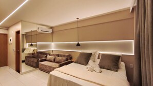 A modern hotel room with a large bed, a sofa, a mirror, and a ceiling-mounted air conditioner. - Malia Beach Experience  (Ipojuca)
