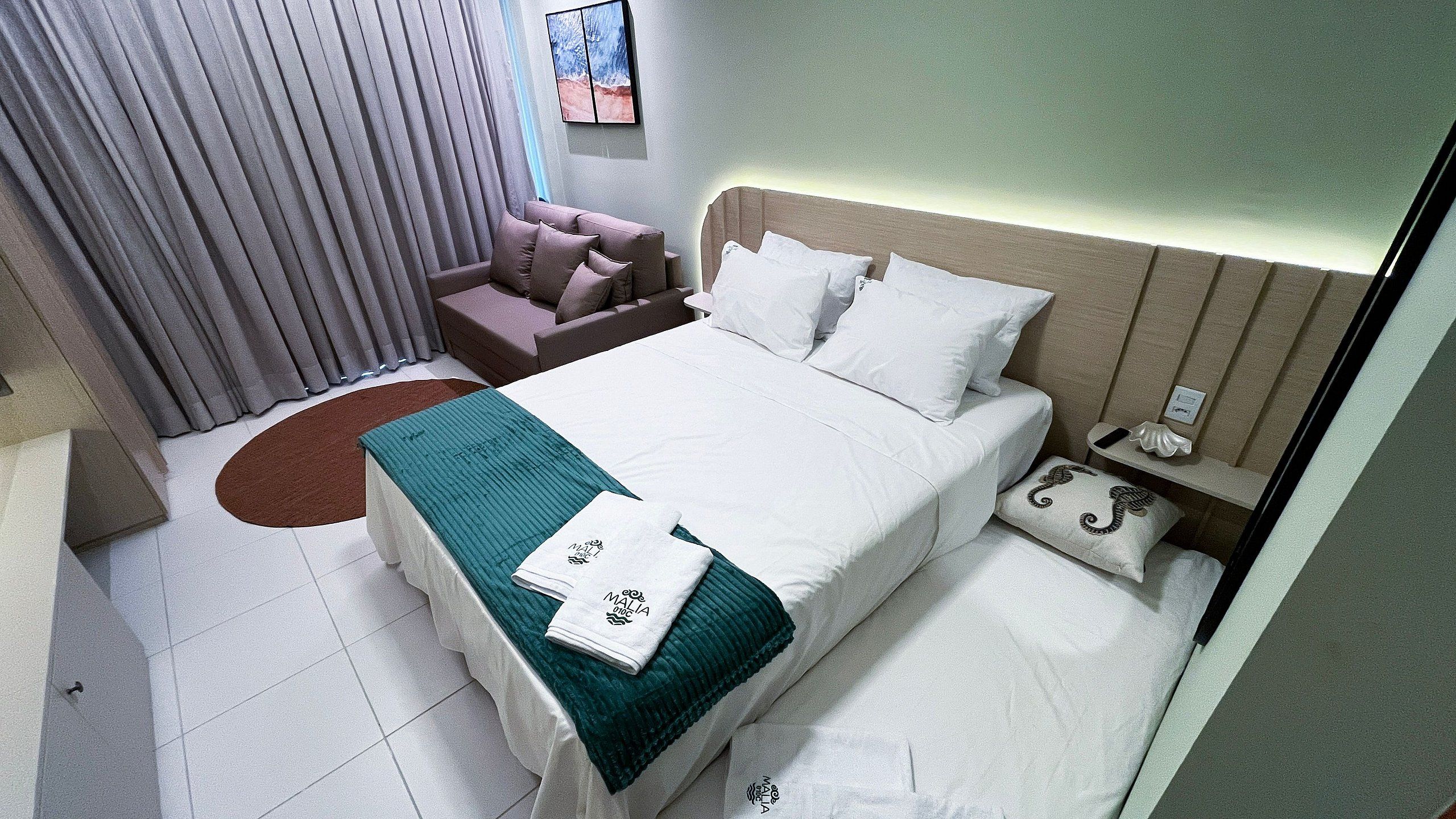 A neatly arranged hotel room with a bed, a sofa, a nightstand, and a wall-mounted painting.