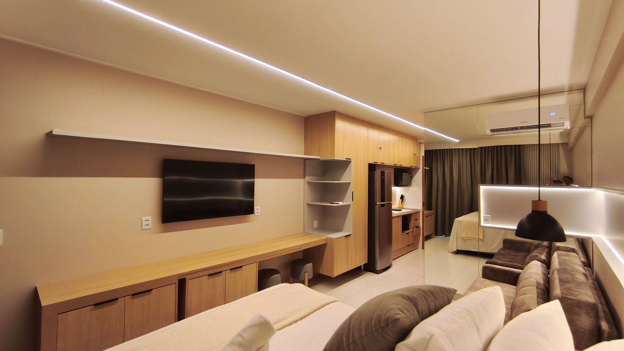 A modern hotel room with a flat-screen TV, wooden furniture, a sofa, and a dining area.