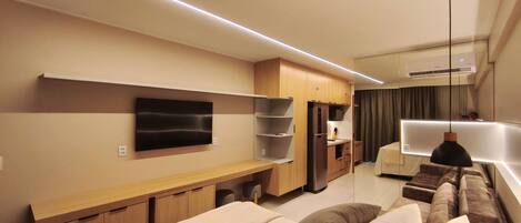 A modern hotel room with a flat-screen TV, wooden furniture, a sofa, and a dining area.