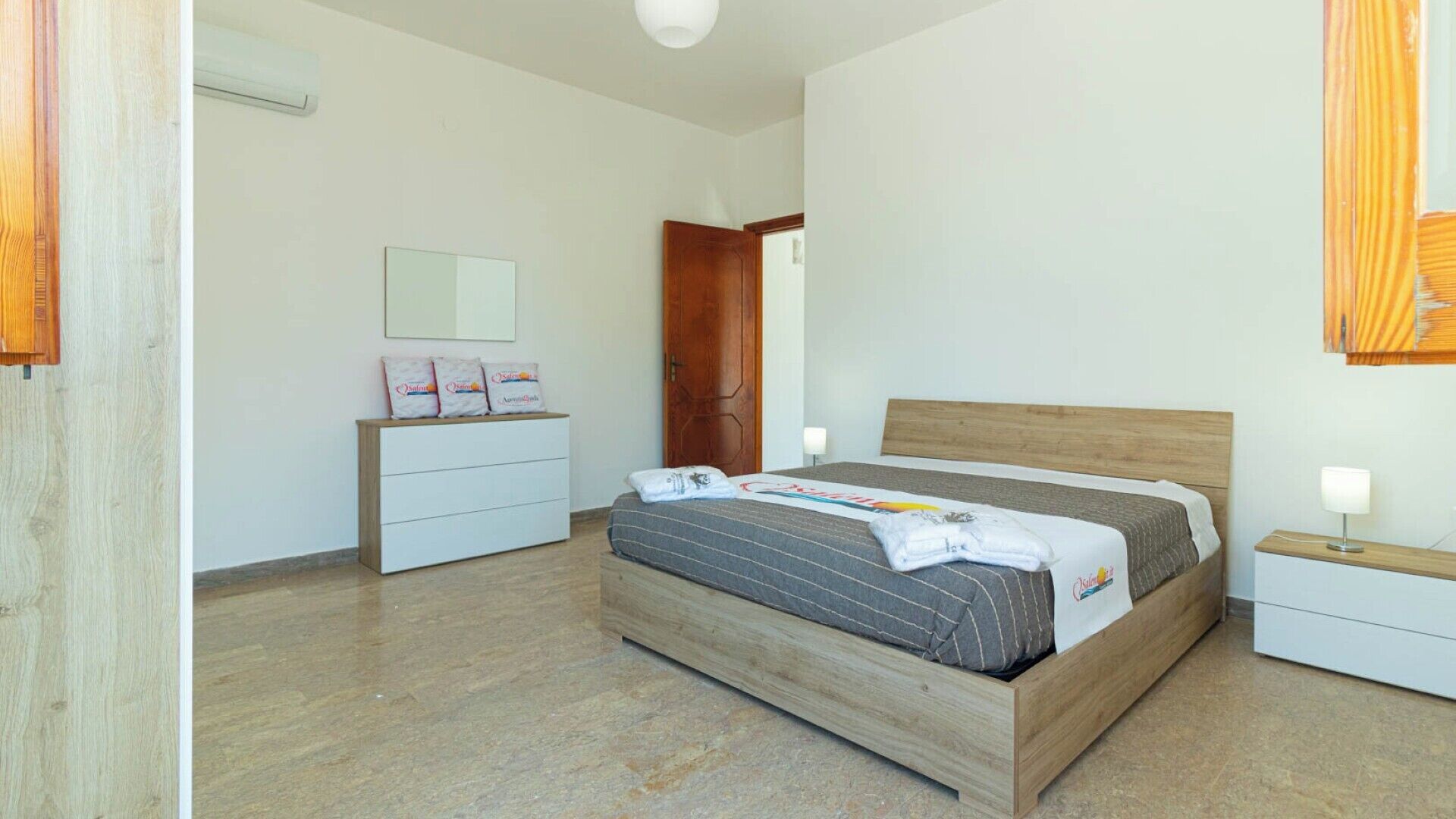 Un dormitorio con una cama de madera, un aparador blanco, una mesita de noche de madera y un espejo en la pared.