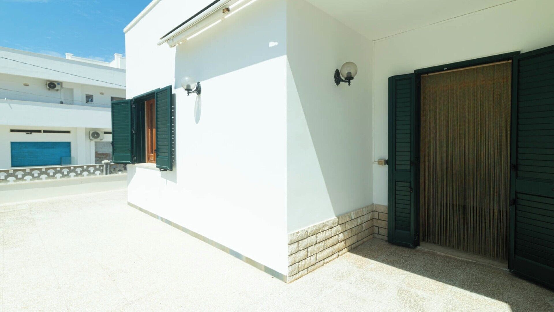 A white building with two green shutters, a tiled entrance, and a closed wooden door.