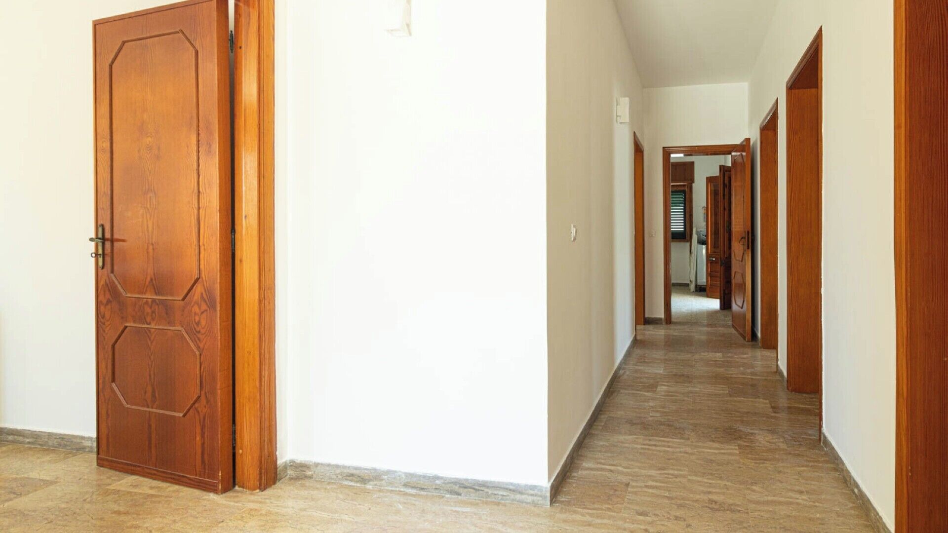 Un couloir avec des portes en bois et un sol carrelé.
