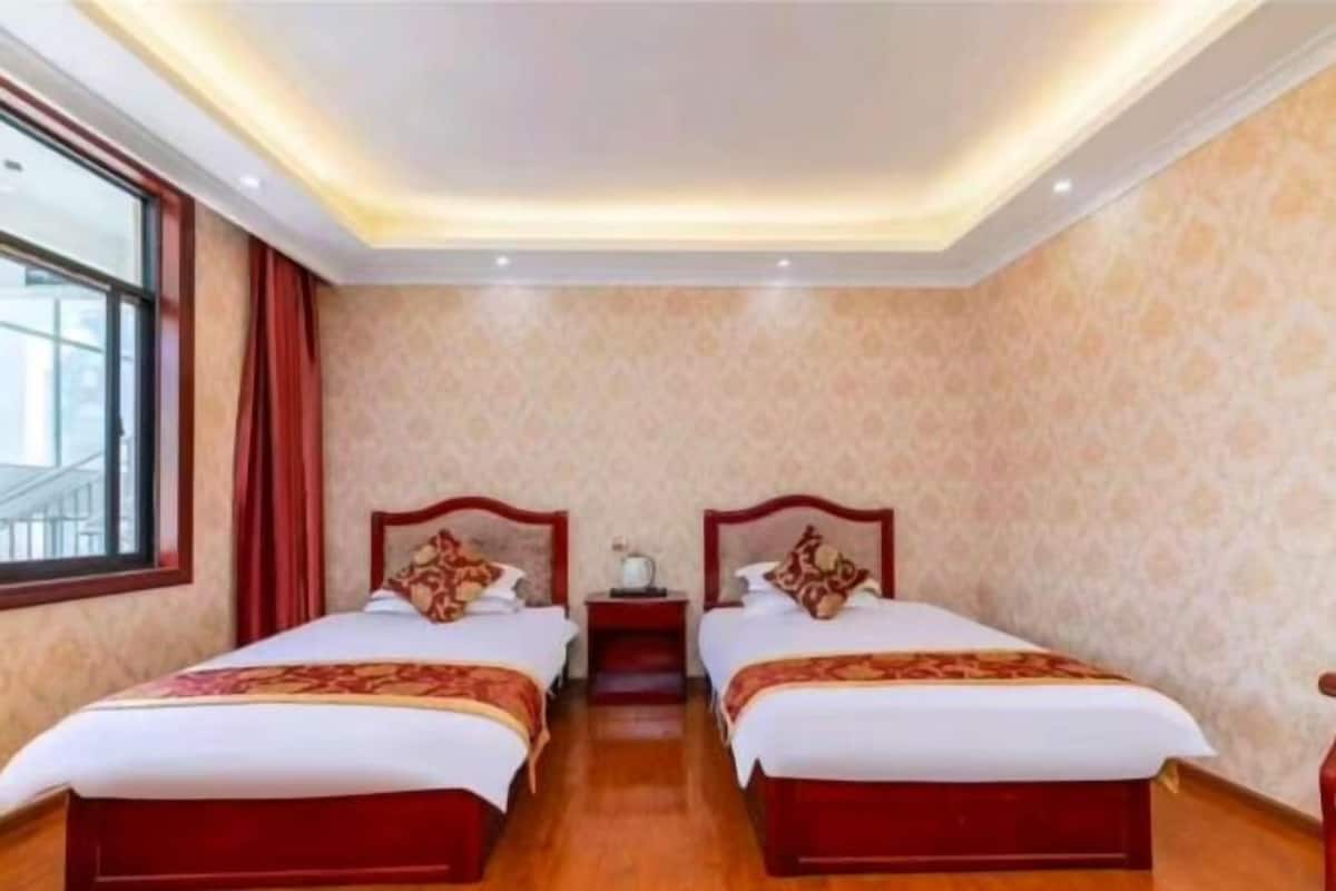 A hotel room with two beds, a window, a nightstand, and a ceiling light.