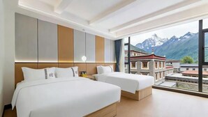 Ett hotellrum med två sängar, ett stort fönster med utsikt över bergen och en traditionell byggnad i bakgrunden.
