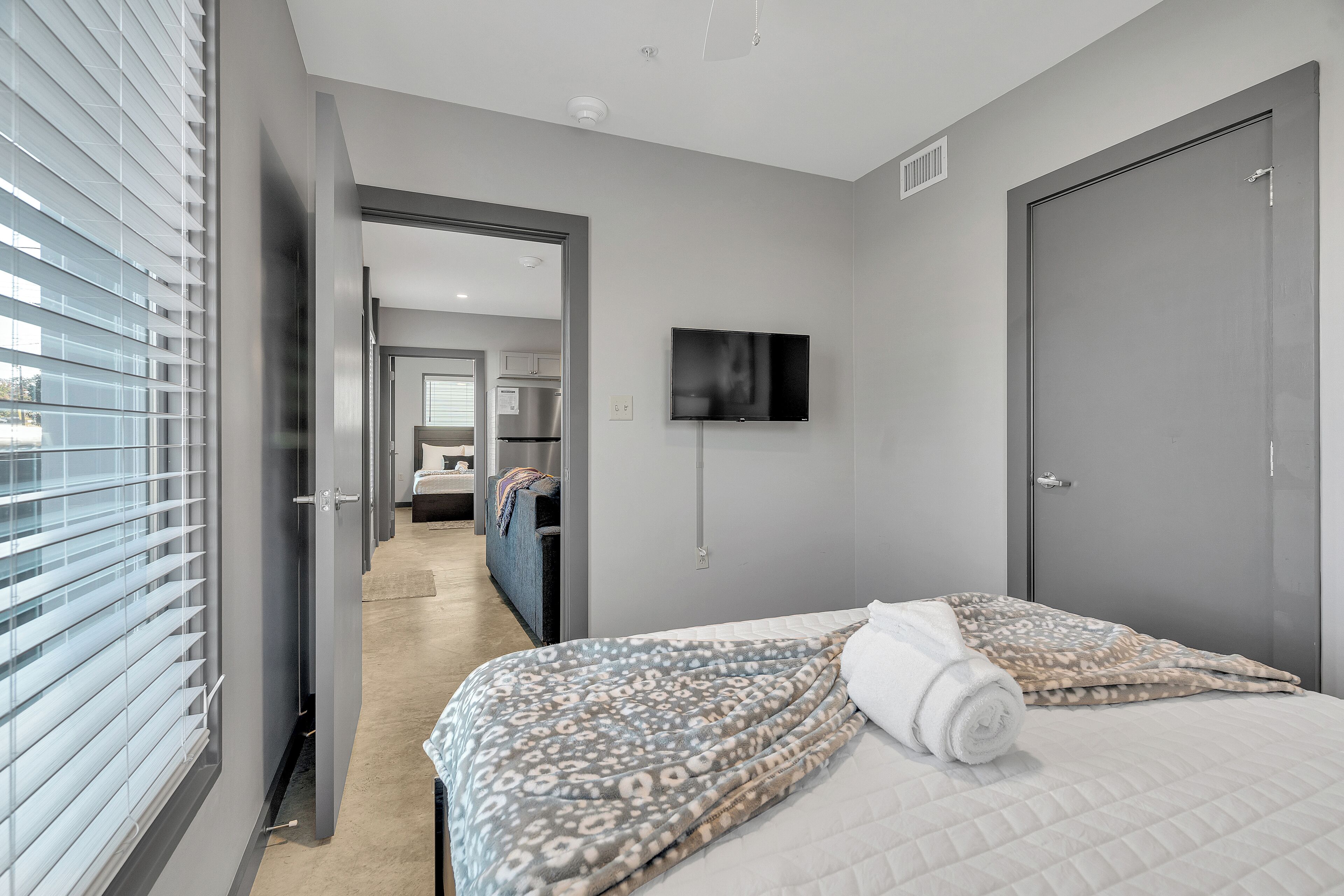 Une chambre d’hôtel moderne dotée d’un grand lit, d’un téléviseur à écran plat et offrant une vue sur le couloir et la cuisine.