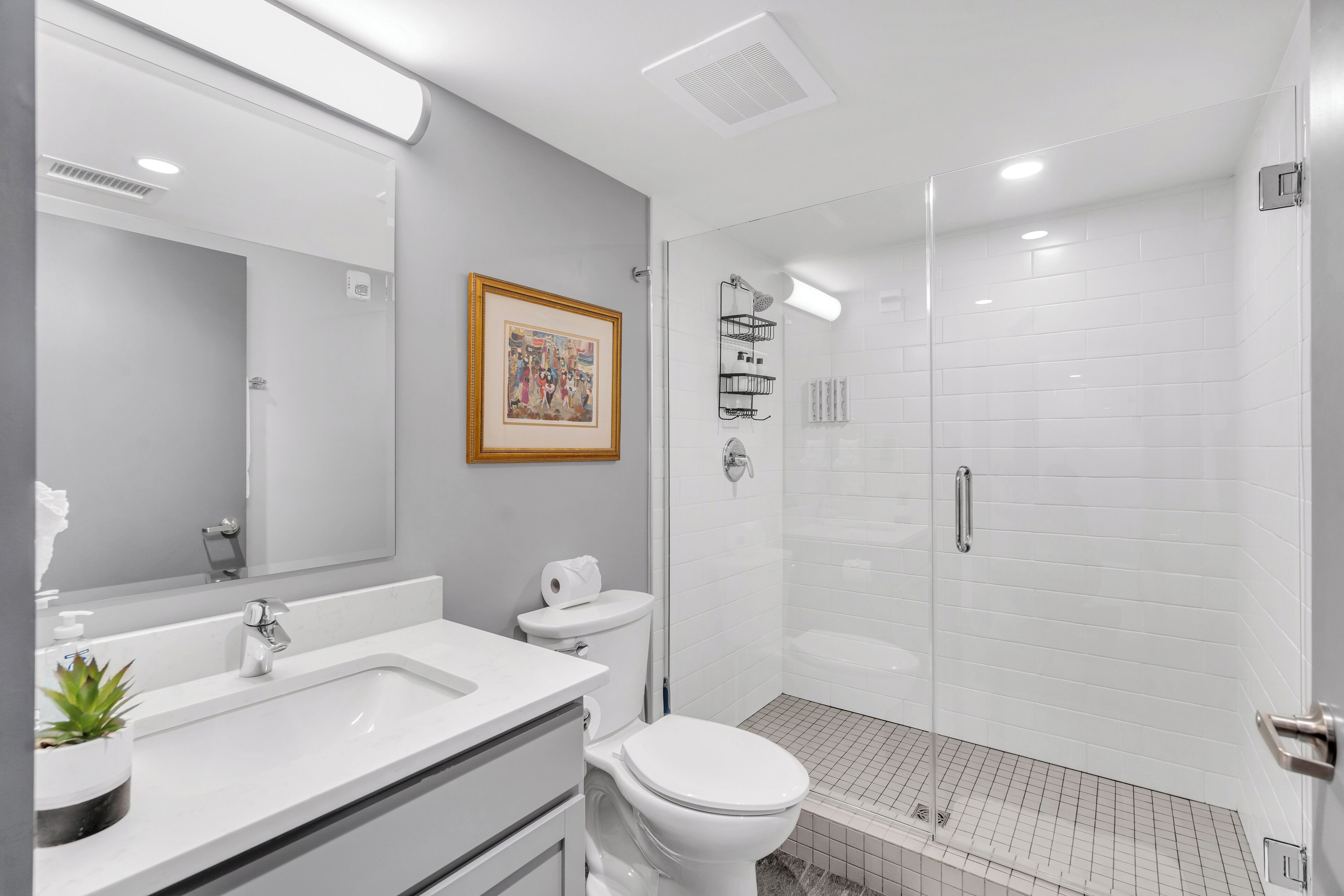 Un baño moderno con lavamanos blanco, inodoro y ducha con mampara de vidrio.
