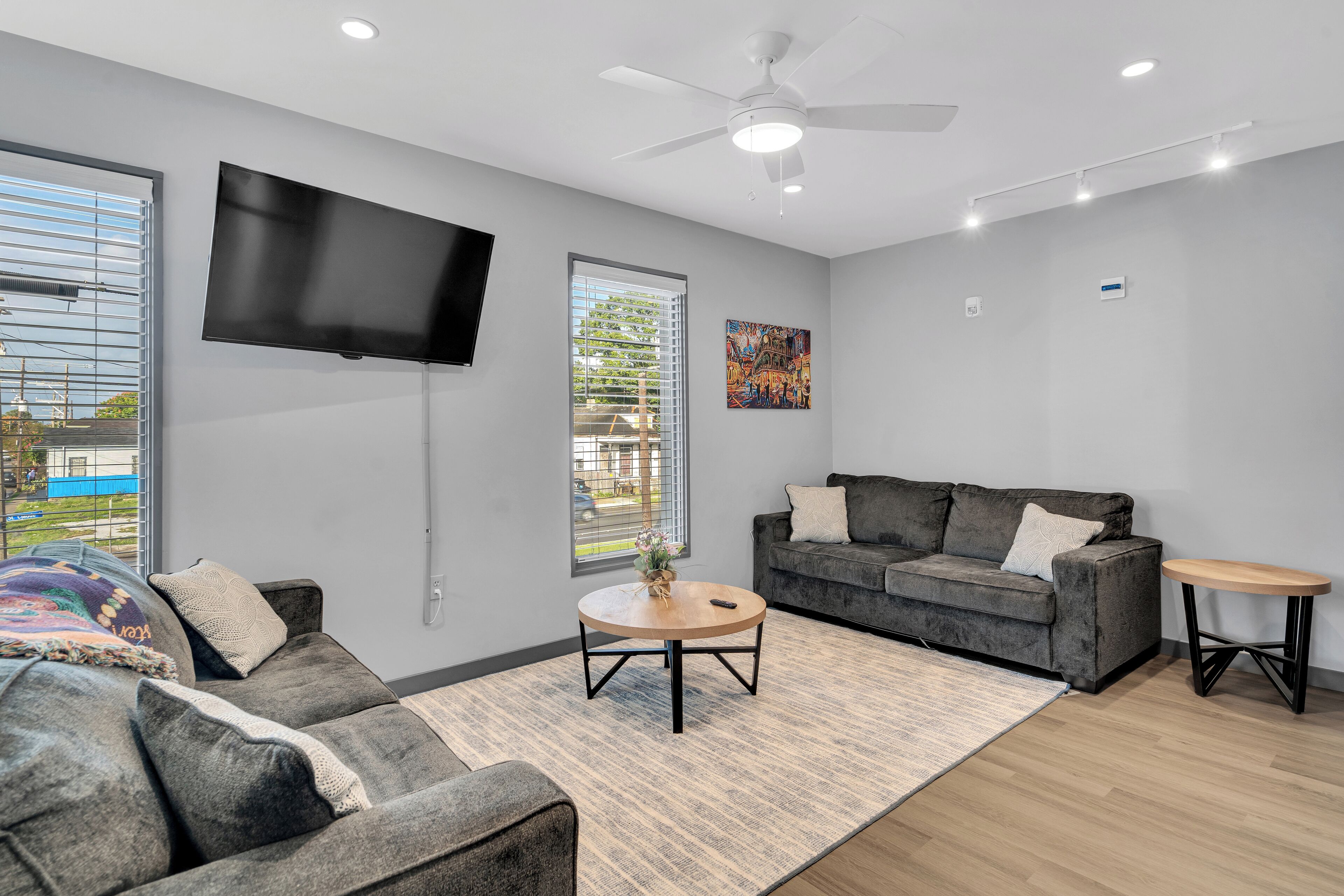 A modern living room with a grey sofa, a round coffee table, and a flat-screen TV mounted on the wall.