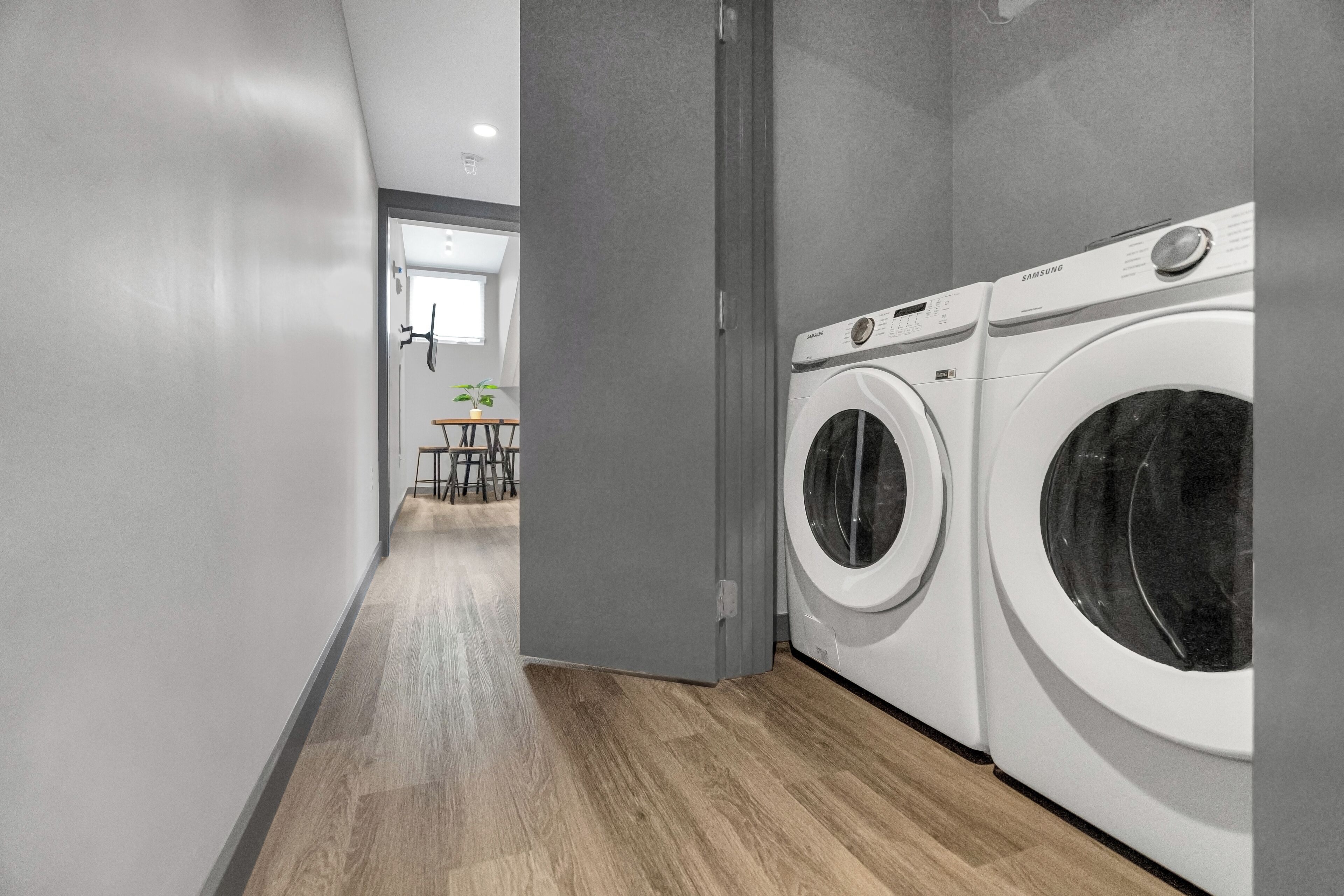 Une buanderie avec deux machines à laver Samsung blanches, un mur gris et un plancher en bois.