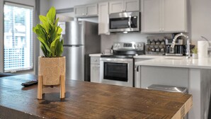 A modern kitchen with white cabinets, stainless steel appliances, and a wooden table with a potted plant. - New Orleans Bywater Apartments (New Orleans)