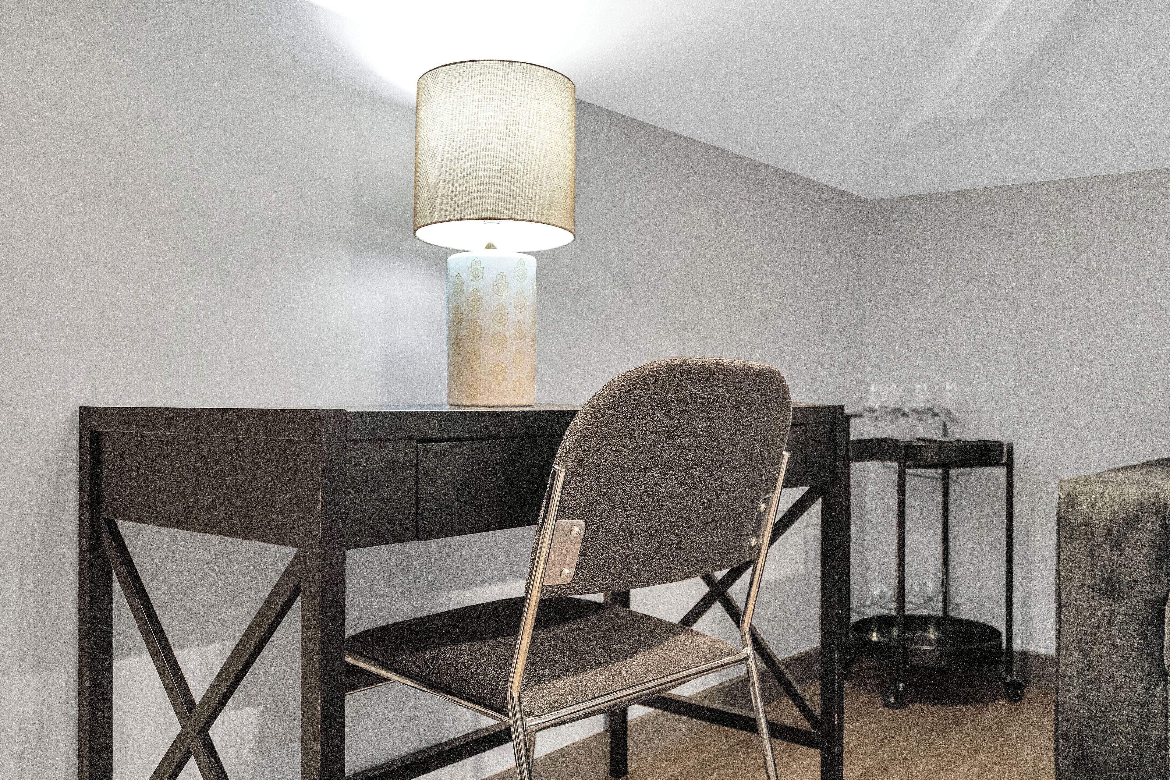 A modern room with a dark wooden desk, a chair with a textured backrest, and a table lamp.