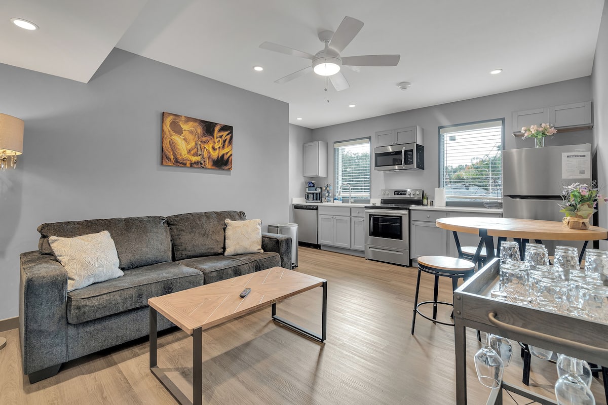 A modern kitchen with stainless steel appliances, a dining area with a bar, and a living room with a sofa and coffee table.