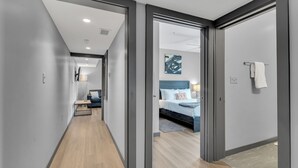 A modern hotel corridor with a wooden floor, a bed with a blue headboard, and a painting on the wall. - New Orleans Bywater Apartments (New Orleans)