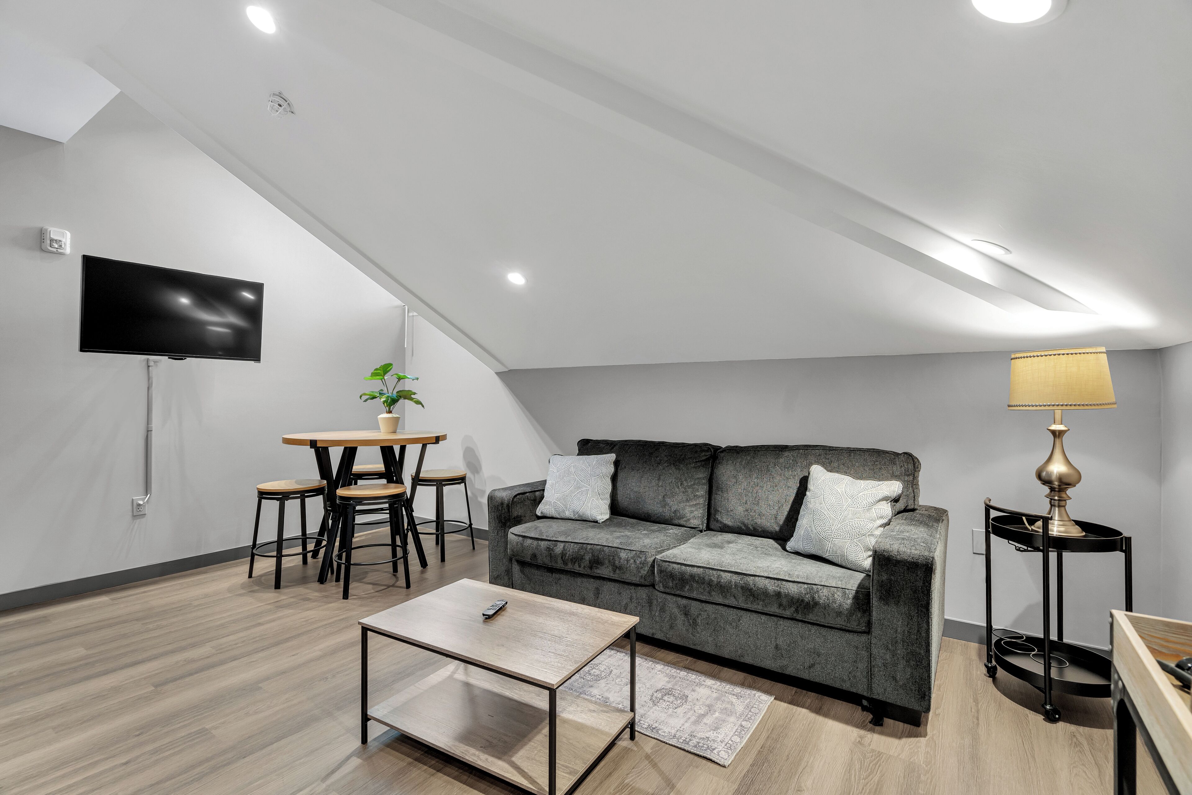 Un salon moderne avec un canapé gris, une table basse, un téléviseur fixé au mur et une lampe sur une table d’appoint.