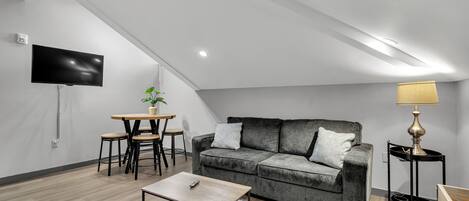 Un salon moderne avec un canapé gris, une table basse, un téléviseur fixé au mur et une lampe sur une table d’appoint.