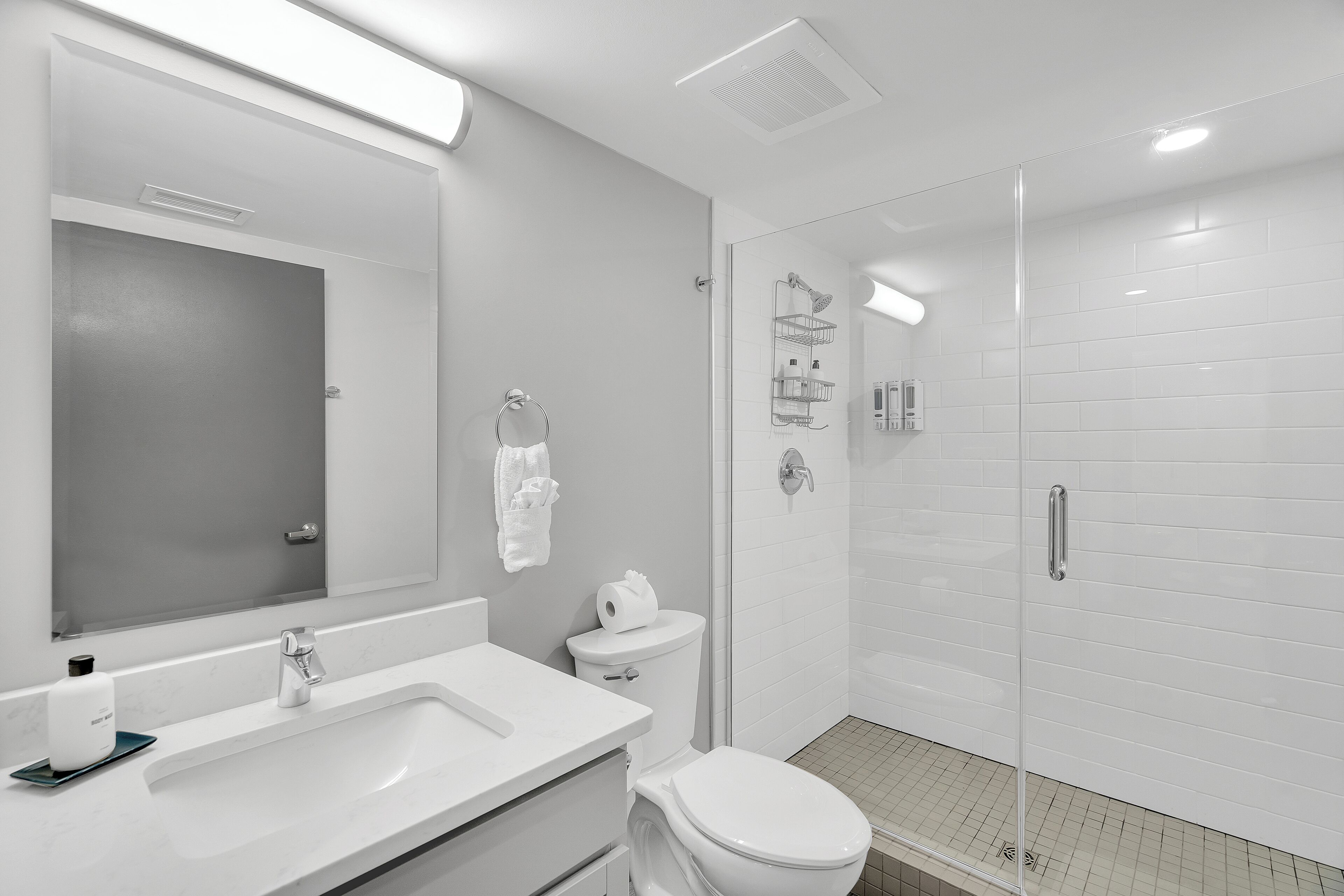A modern bathroom with a large mirror, white sink, and a glass-enclosed shower.