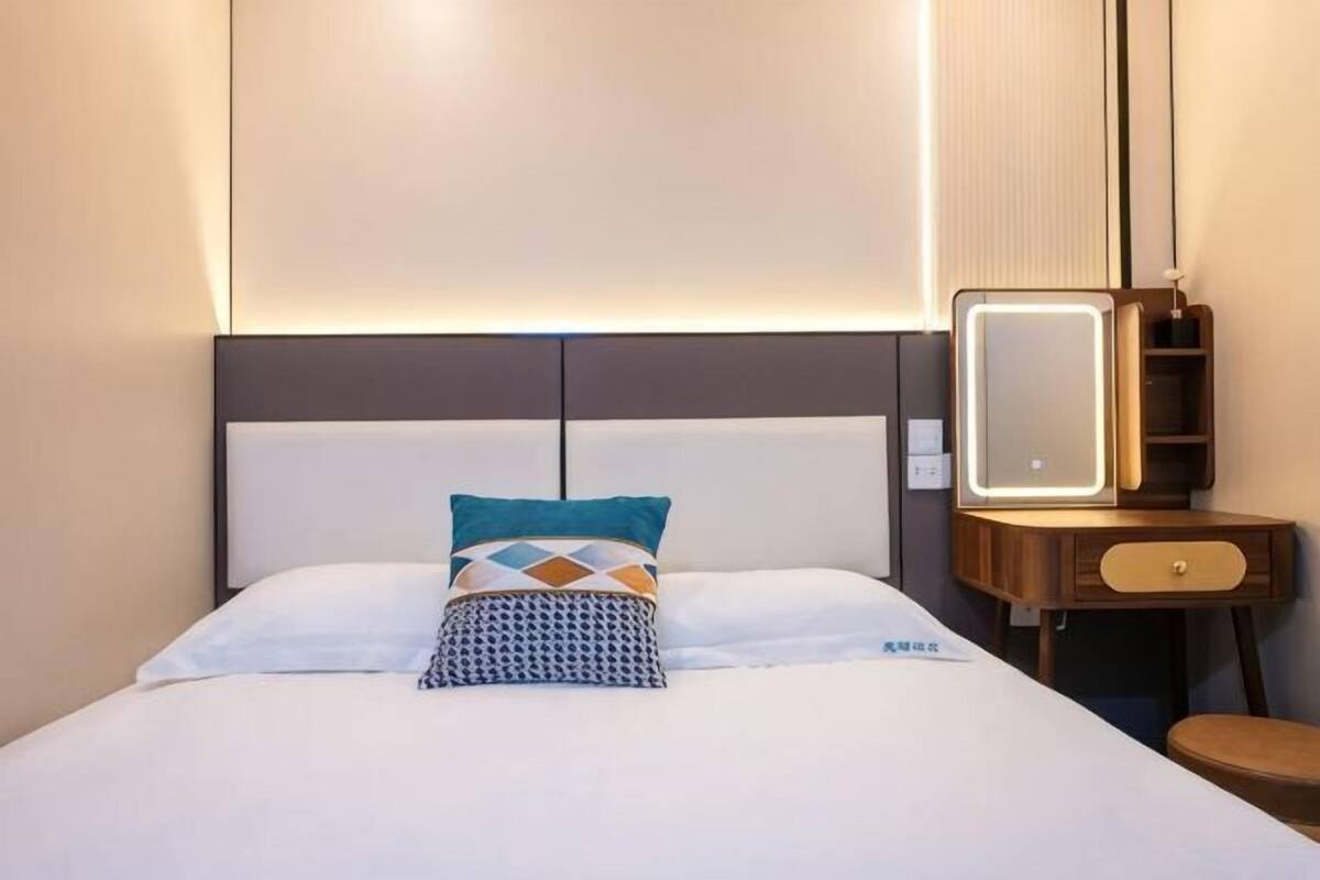 Una habitación de hotel con una cama, una mesita de noche con espejo y una pequeña silla de madera.