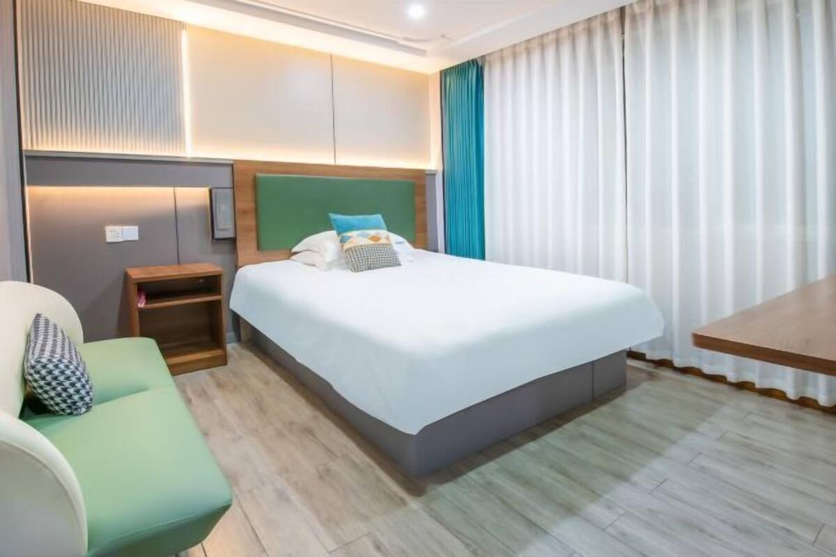 Una habitación de hotel con una cama, una silla verde, una mesita de noche de madera y una mesa de madera.