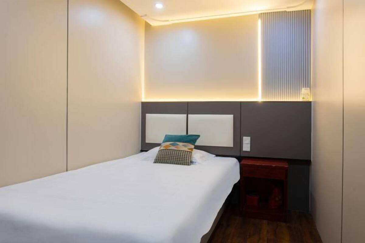 Una habitación de hotel moderna con una cama bien hecha, una mesita de noche y un aplique en la pared.