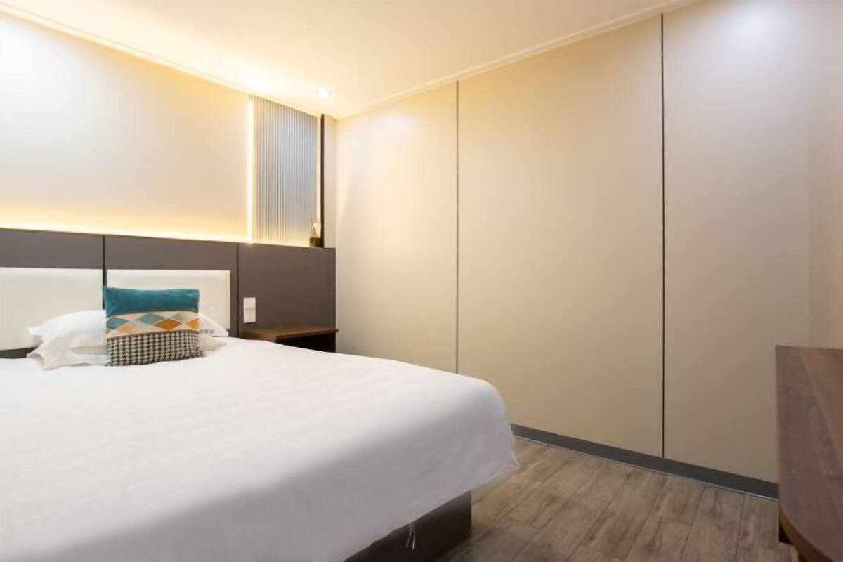 Una habitación de hotel moderna con una cama bien hecha, una mesita de noche y un armario.