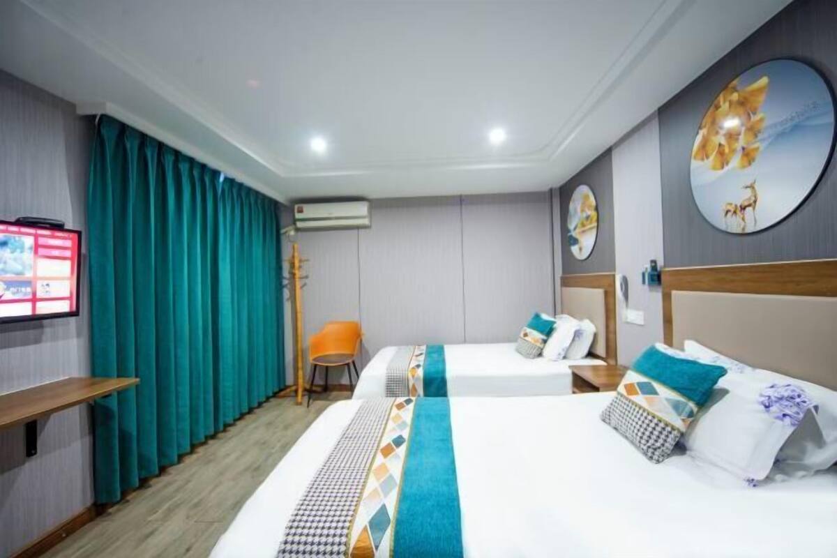 Habitación de hotel con dos camas, cortinas color turquesa, televisor y aire acondicionado instalado en la pared.