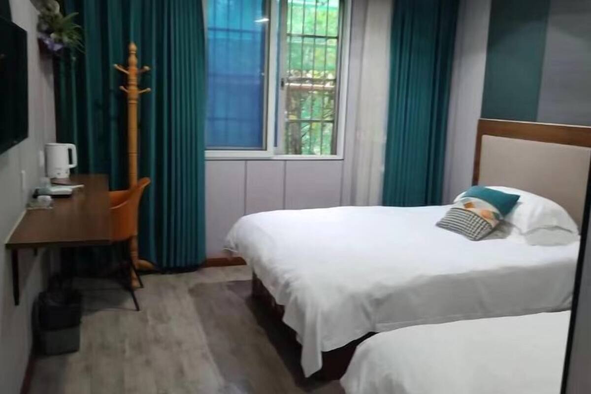 Habitación de hotel con dos camas, un escritorio, una silla y una ventana con cortinas.