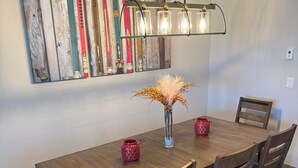 A dining area with a wooden table, six chairs, a vase with dried flowers, and a wall-mounted surfboard art piece. - Spacious Mountain Retreat on Golf Course, near Rocky Mountain National Park (Granby)