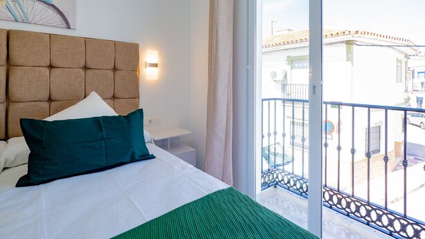 A hotel room with a large bed, a headboard, a wall-mounted light, and a view of the outside balcony. - Cubo’s La Perla Town Center House / urban / air conditioning / free Wi-Fi (Alhaurín el Grande)