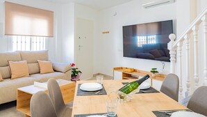 A modern living room with a sofa, dining table, and chairs. A TV is mounted on the wall, and there is a staircase to the right. - Cubo’s La Perla Town Center House / urban / air conditioning / free Wi-Fi (Alhaurín el Grande)