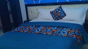 Ein Schlafzimmer mit Wand in geometrischem Muster, einem Bett mit farbenfroher Tagesdecke und einem Spiegel an der Wand.
