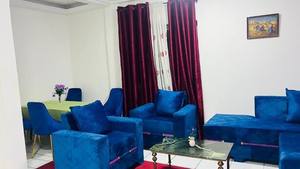 Ein Wohnzimmer mit blauen Sofas, einem roten Teppich und einem Essbereich mit einem grünen Tisch und Stühlen.