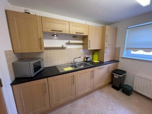 A kitchen with wooden cabinets, a microwave, a sink, and a trash bin. - 3 Bed Flat - Sleeps 6 - Parking - Wifi (Aberdeen)