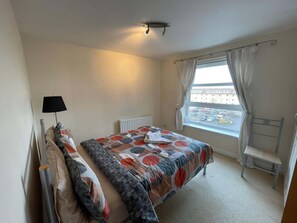 A bedroom with a bed, a radiator, a window with curtains, a chair, and a lamp. - 3 Bed Flat - Sleeps 6 - Parking - Wifi (Aberdeen)