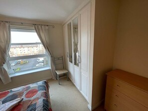A bedroom with a bed, a dresser, a window with curtains, and a view of the street. - 3 Bed Flat - Sleeps 6 - Parking - Wifi (Aberdeen)