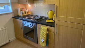 A kitchen with wooden cabinets, a gas stove, an oven, and a yellow kettle. - 3 Bed Flat - Sleeps 6 - Parking - Wifi (Aberdeen)