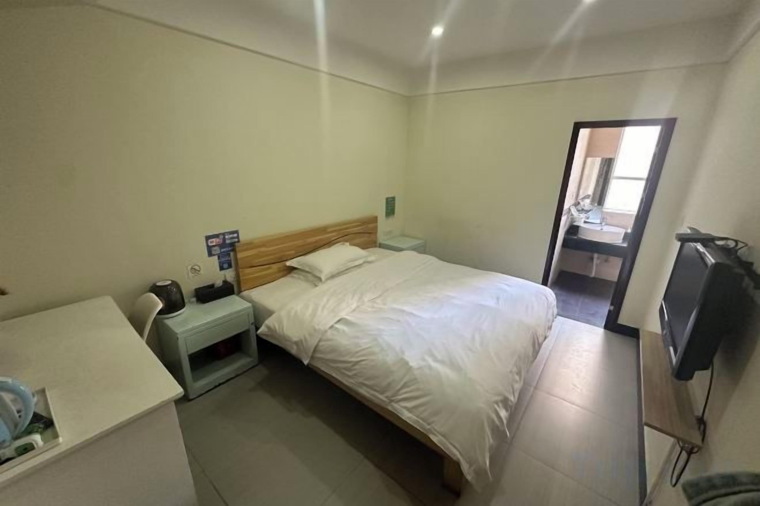 A hotel room with a bed, a desk, a nightstand, and a television.