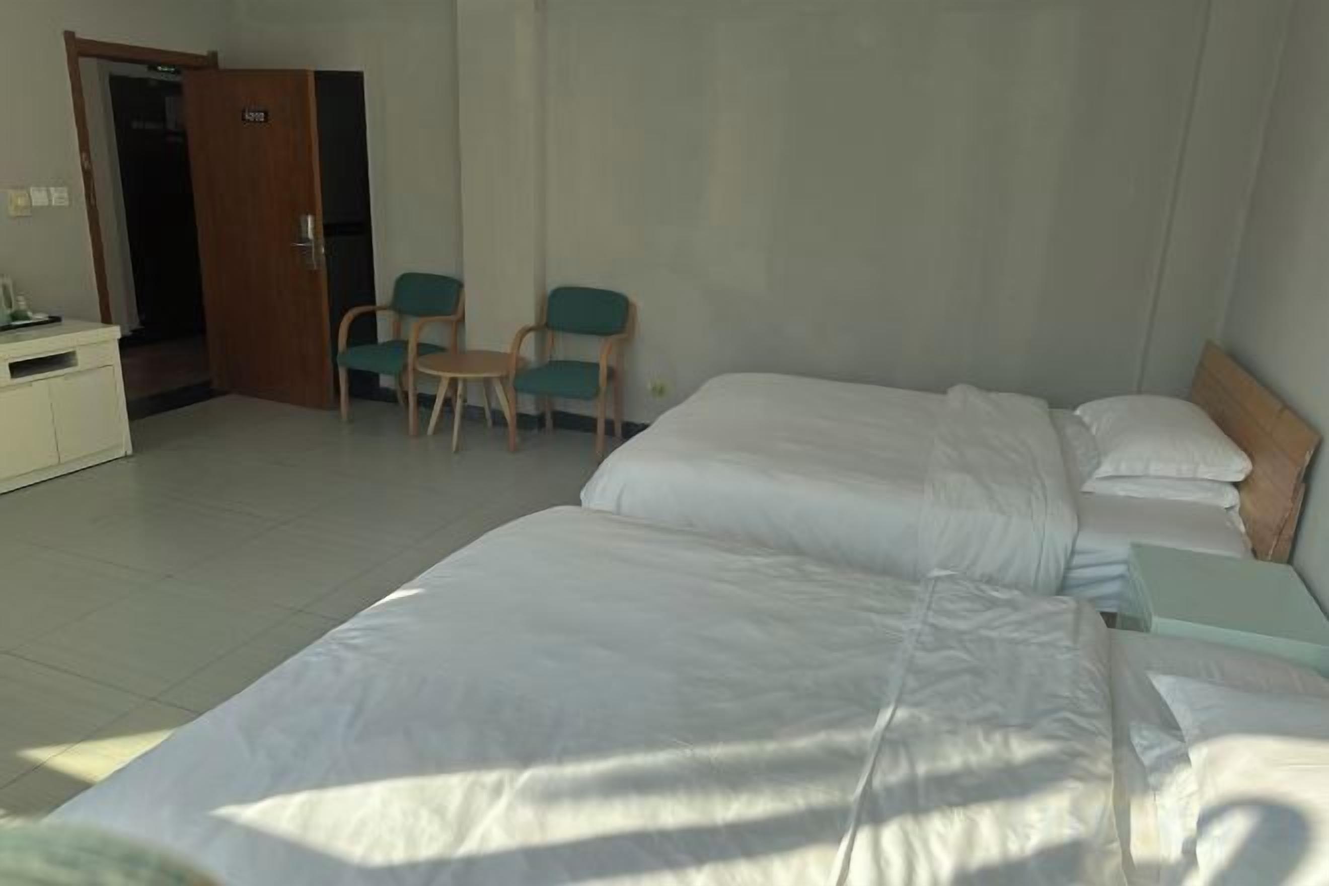 A hotel room with two beds, a desk, a chair, and a wardrobe.
