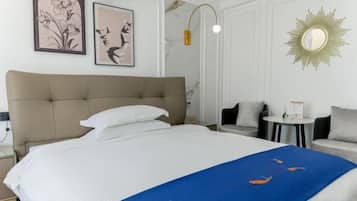 A hotel room with a large bed, a bedside table, a small round table, and a sofa.