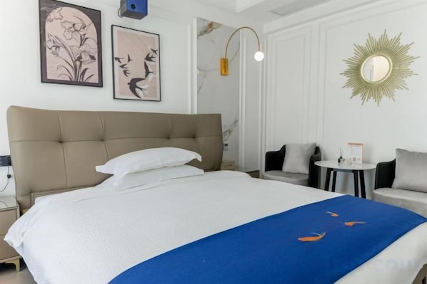 A hotel room with a large bed, a bedside table, a small round table, and a sofa.