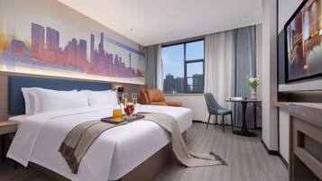 A hotel room with a large bed, a TV, a desk with a chair, and a window with a city view.