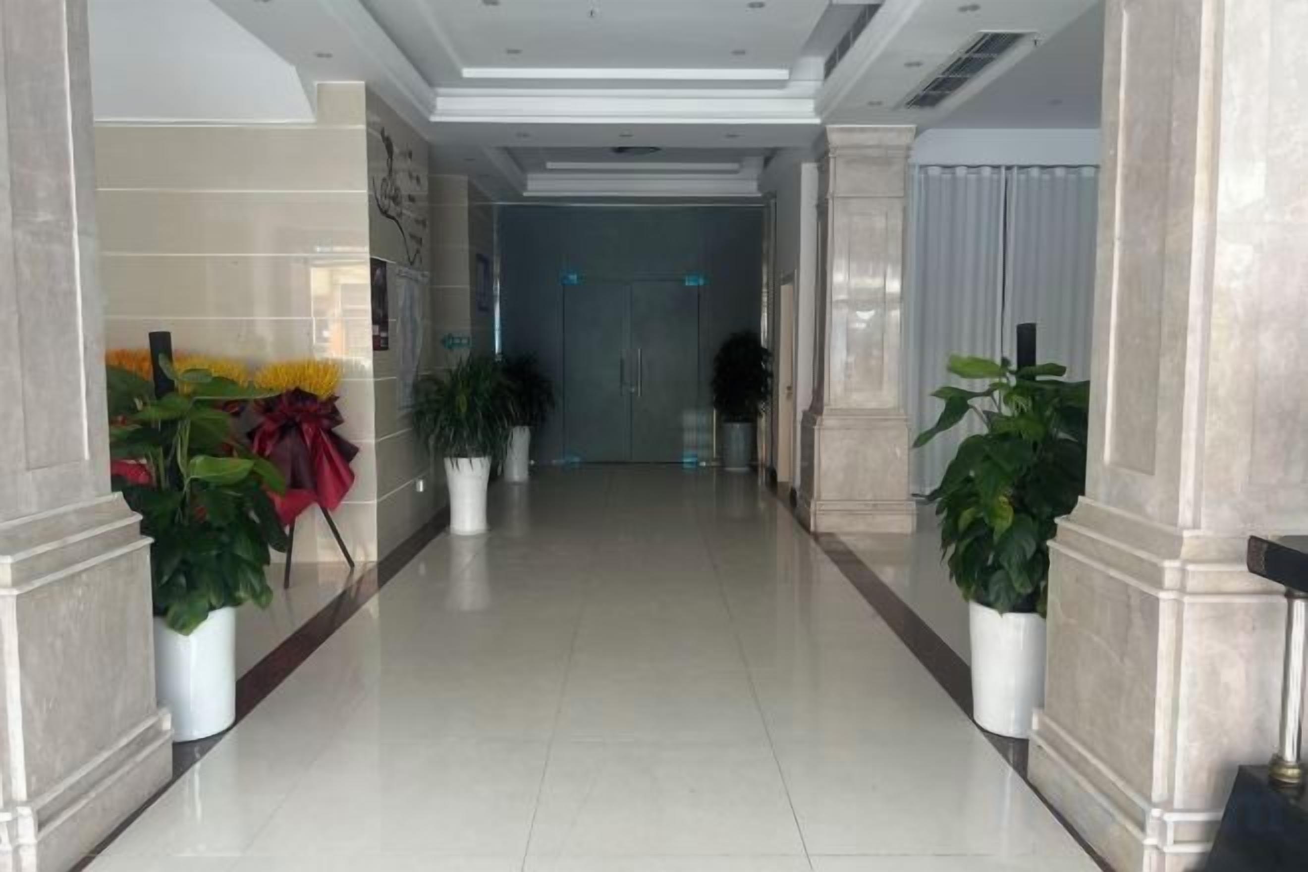 A hallway with potted plants, a door at the end, and a tiled floor.