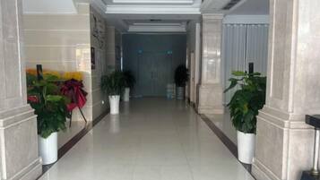 A hallway with potted plants, a door at the end, and a tiled floor.